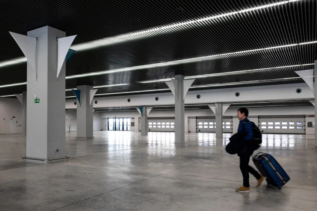 A traveler with a wheeled suitcase walking through a modern airport terminal